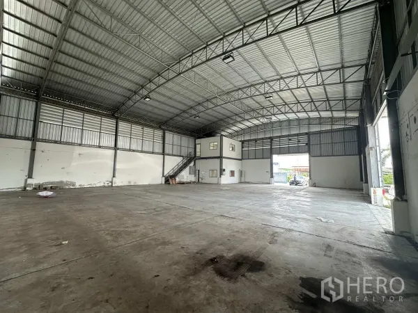 Factory for rent in Pathum Thani - Spacious warehouse interior with high steel truss roof, concrete floor and mezzanine office.