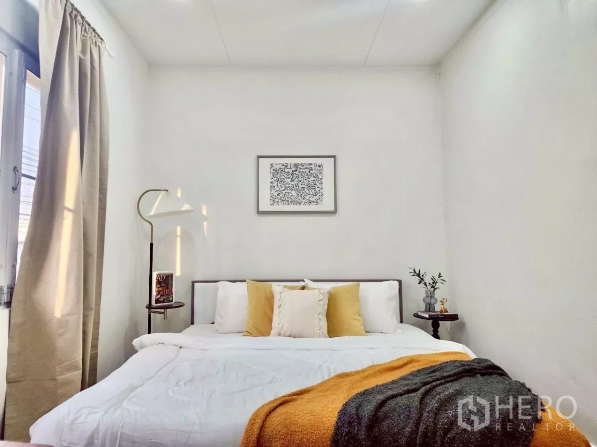 Detached House for rent in Chatuchak, Bangkok - Cozy bedroom with soft lighting, white bedding and mustard accent throw.