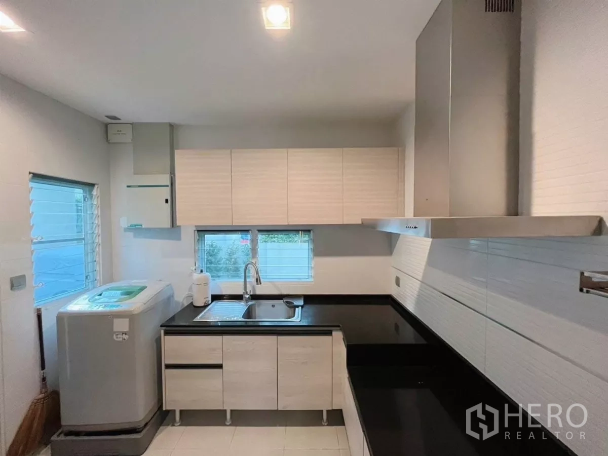 Detached House for rent in Samut Prakan - Compact modern kitchen with white cabinets, black countertops, sink, and range hood.
