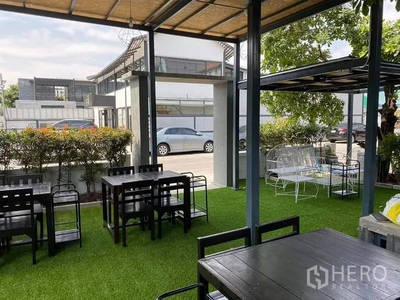 Retail Space for rent in Suan Luang, Bangkok - Covered outdoor seating terrace with artificial lawn, black tables, and access to the adjacent parking area.