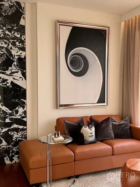 Condominium for sale in Watthana, Bangkok - Contemporary living area featuring a tan leather sofa, spiral abstract artwork and a marble accent wall.