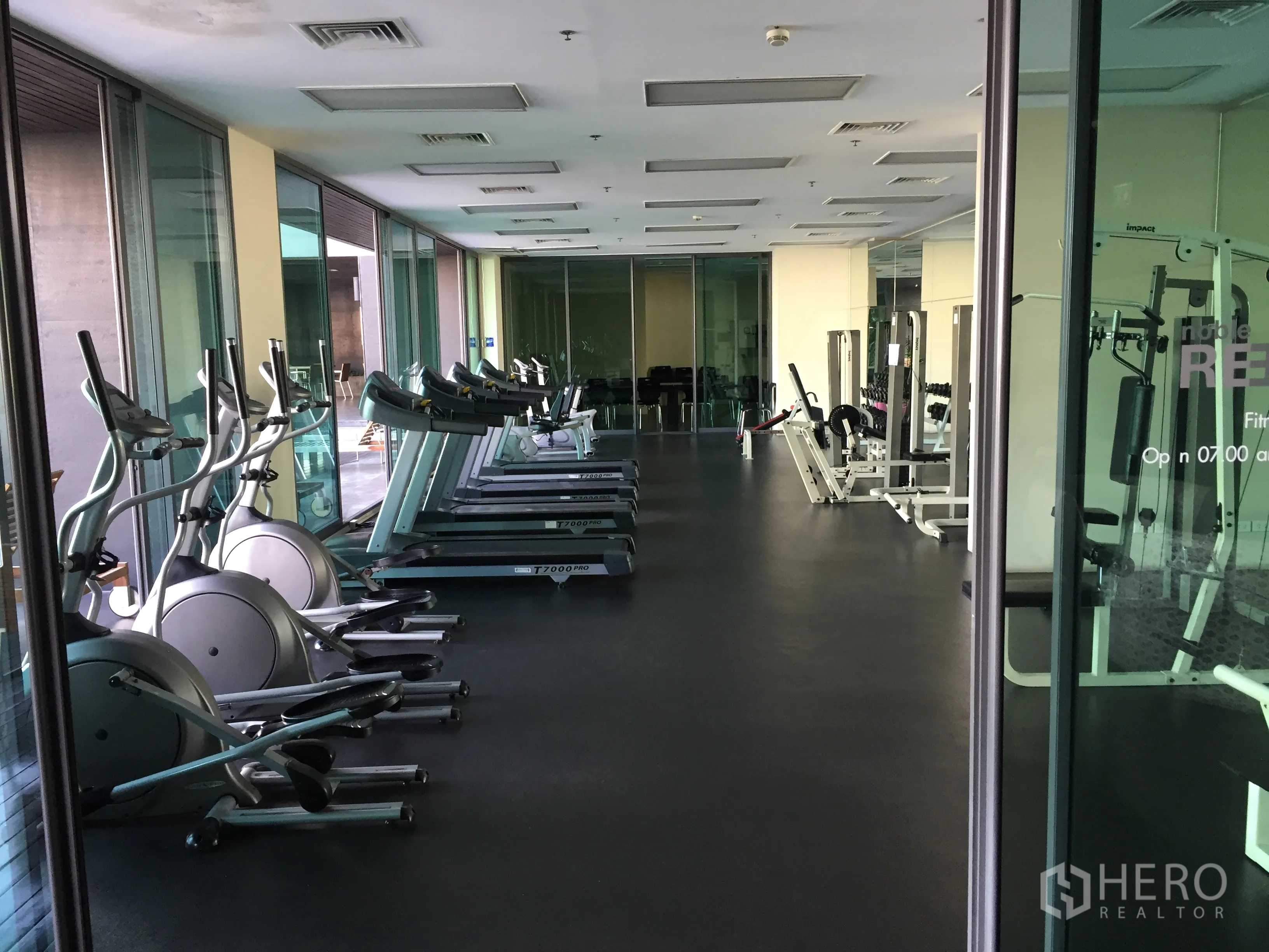 Condominium for rent in Khlong Toei, Bangkok - Condo fitness center with treadmills, ellipticals and weight machines behind glass walls.