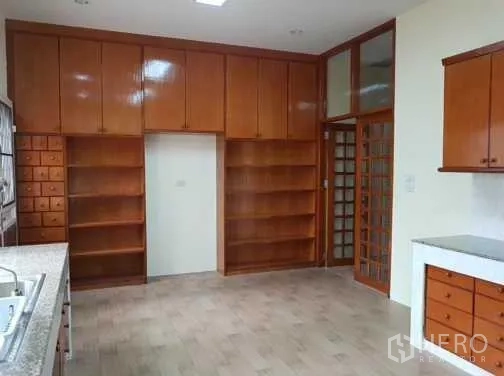 Townhouse for rent in Khlong Toei, Bangkok - Kitchen with extensive wooden cabinetry and open shelving for storage.