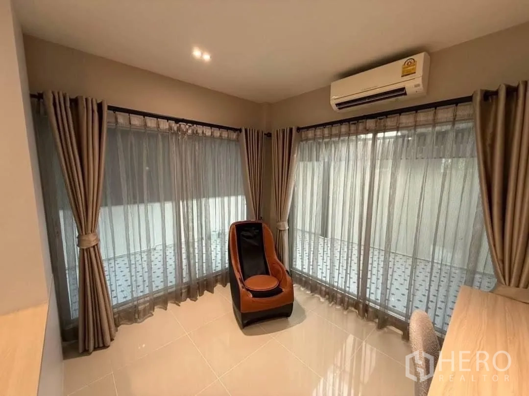 Detached House for rent in Prawet, Bangkok - Corner sitting room with massage chair, wraparound windows and curtains.