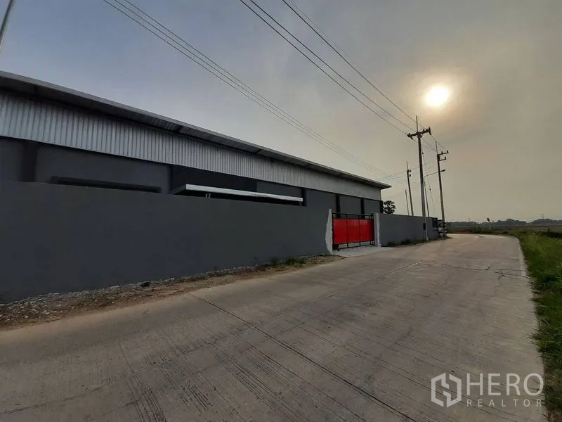 คลังสินค้า ให้เช่าในLam Luk Ka, Pathum Thani - มุมมองถนนคอนกรีตหน้าทรัพย์ กำแพงโกดังและประตูสีแดง