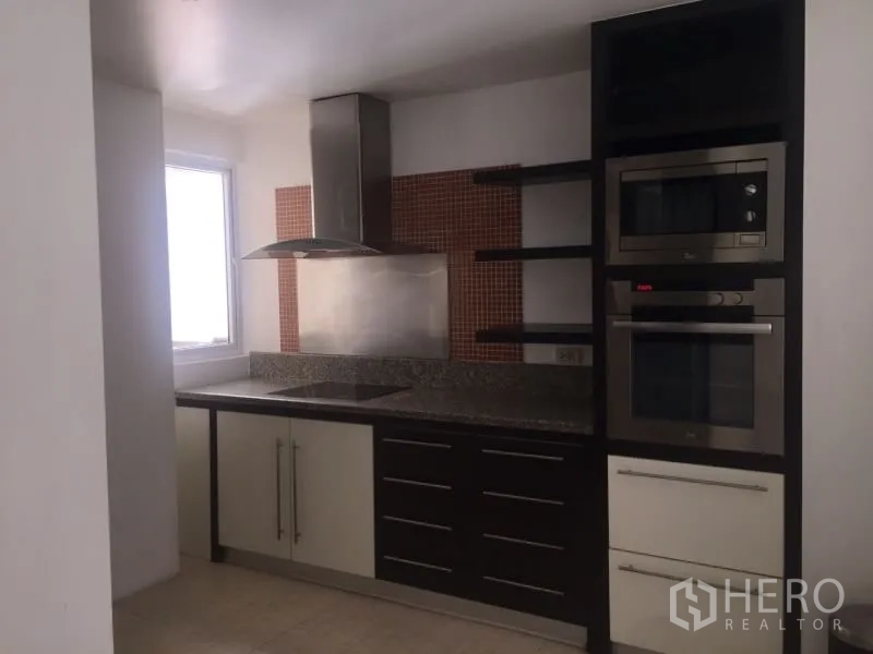 Condominium for rent in Watthana, Bangkok - Modern condo kitchen with granite countertops, induction hob, range hood, and built-in oven and microwave.