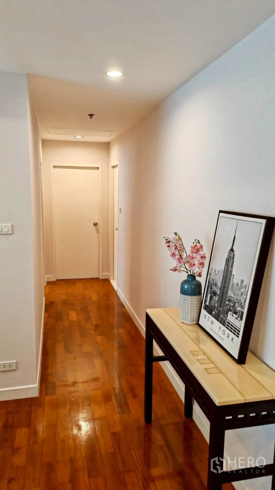 Condominium for rent in Khlong Toei, Bangkok - Hallway with wooden floors and a console table with artwork.