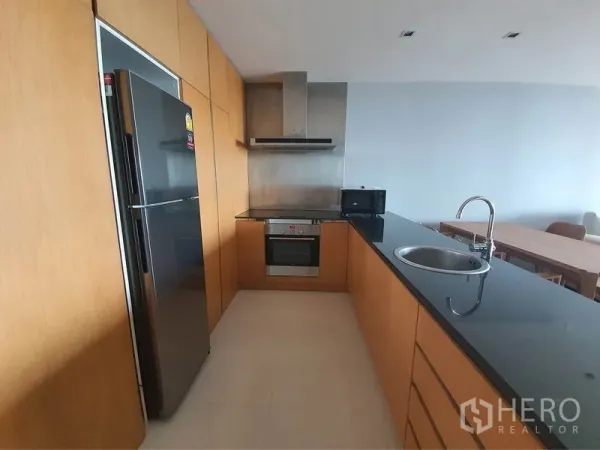 Condominium for rent in Yan Nawa, Bangkok - Modern kitchen with black granite countertop, built-in oven, hood and stainless fridge.