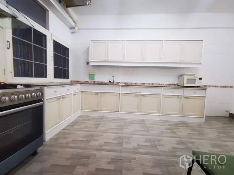 房间 出租在Khlong Toei, Bangkok - 宽敞厨房，长排白色橱柜、燃气炉与仿木地砖。