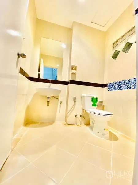 联排别墅 出租在Prawet, Bangkok - 整洁的瓷砖卫浴，马桶、台盆、镜子与蓝色马赛克装饰。