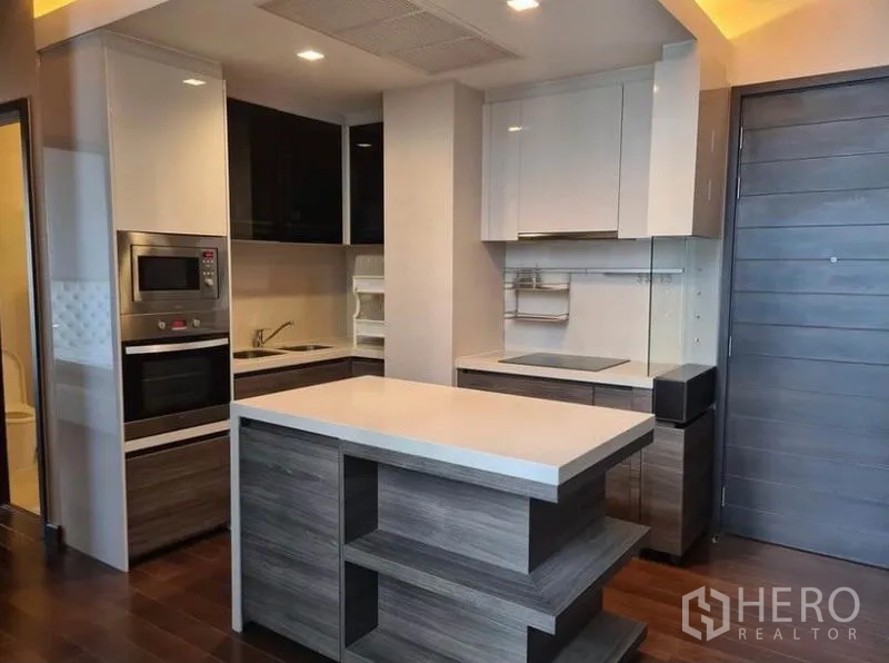 Condominium for rent or sale in Huai Khwang, Bangkok - Modern kitchen with island, built-in oven and sleek wood-and-white cabinetry.
