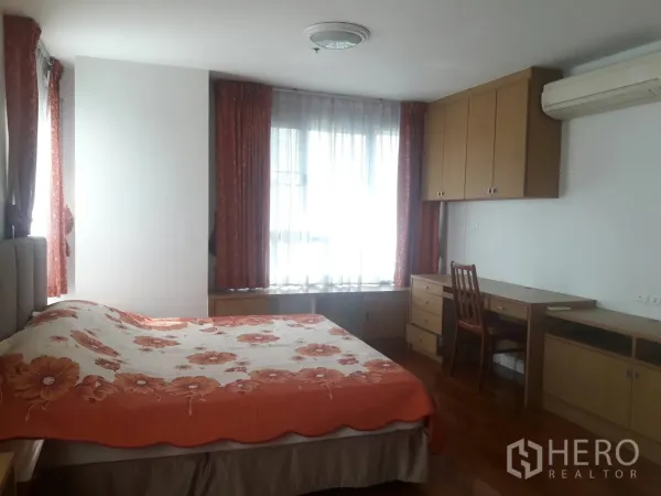 คอนโด ให้เช่าในKhlong Toei, Bangkok - ห้องนอนหลักสว่าง มีหน้าต่างบานใหญ่ โต๊ะทำงานและตู้บิวท์อิน เครื่องปรับอากาศ และผ้าคลุมลายดอก