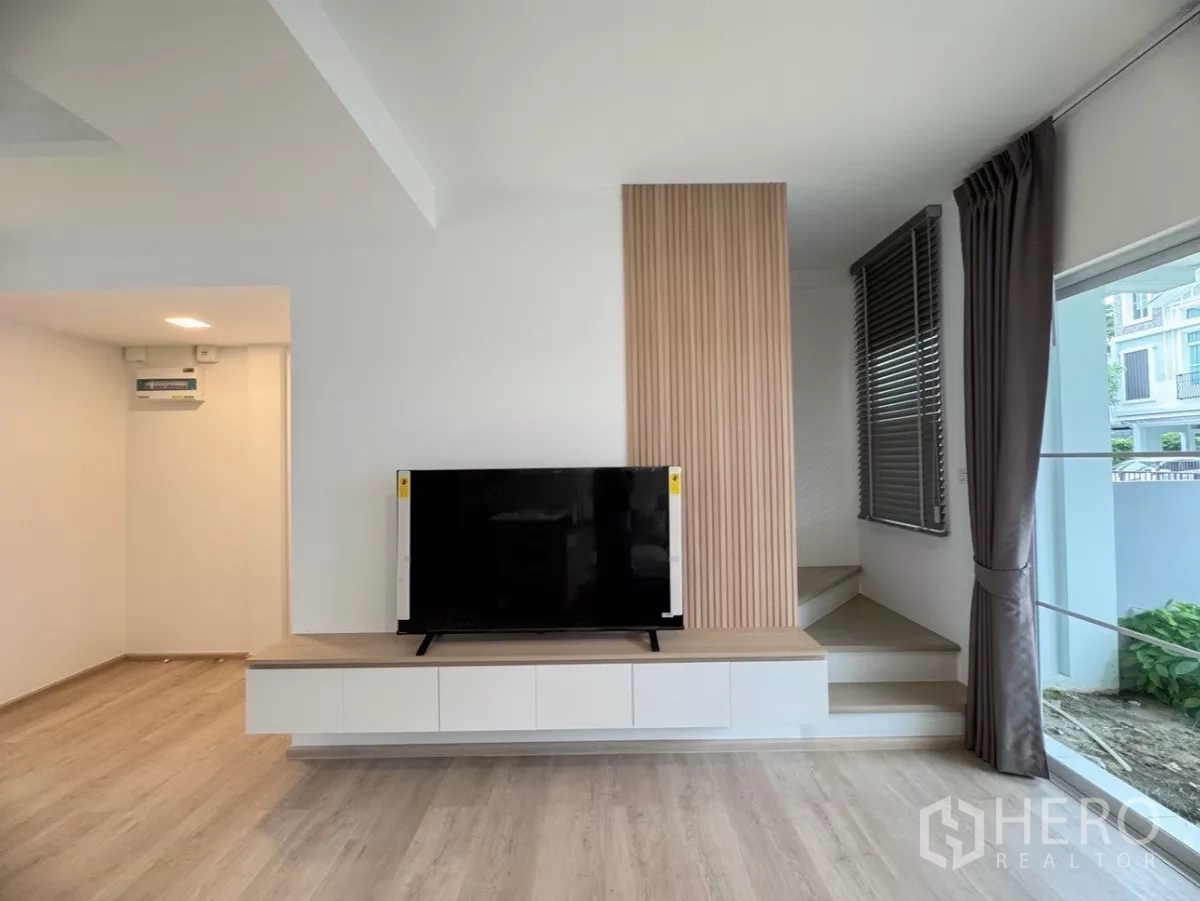 联排别墅 出租在Prawet, Bangkok - 电视柜与通往二层的台阶，侧窗配窗帘。