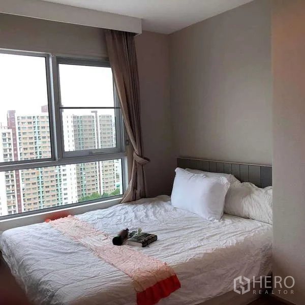Condominium for sale in Huai Khwang, Bangkok - Corner bedroom with double bed and two-side windows overlooking the city skyline.