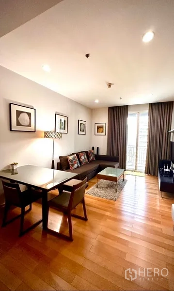 Condominium for rent or sale in Watthana, Bangkok - Open-plan lounge and dining with sofa, framed art and sliding door to the balcony with blackout curtains.