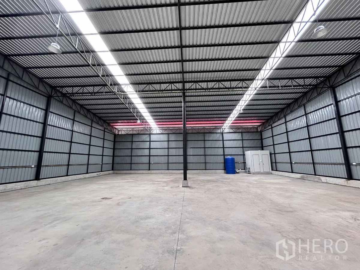 Warehouse for rent in Khlong Toei, Bangkok - Spacious 400 sq.m warehouse interior with 7 m high steel-truss ceiling, bright strip lighting, concrete floor, and restrooms with water tank at the rear.