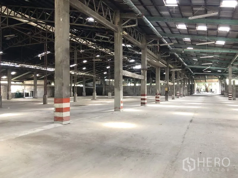 คลังสินค้า ให้เช่าในThanyaburi, Pathum Thani - ภายในโกดังขนาดใหญ่ พื้นคอนกรีต หลังคาโครงเหล็กสูง มีช่องแสง และเสาคาดแถบสีเพื่อความปลอดภัย