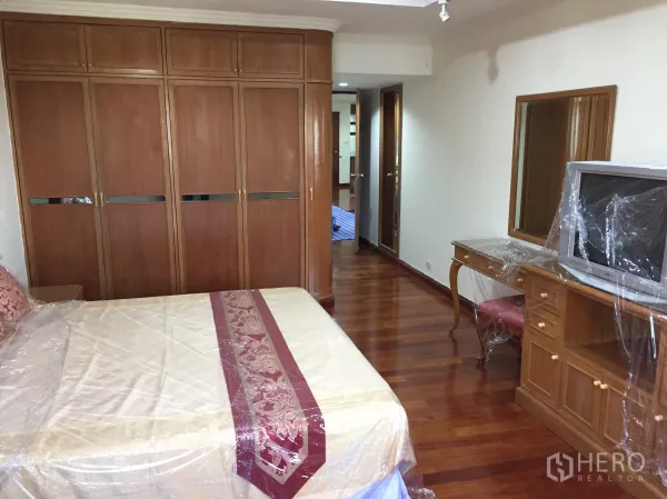 Condominium for rent in Watthana, Bangkok - Primary bedroom with wooden floors, large built-in wardrobes, dressing table, and a double bed.