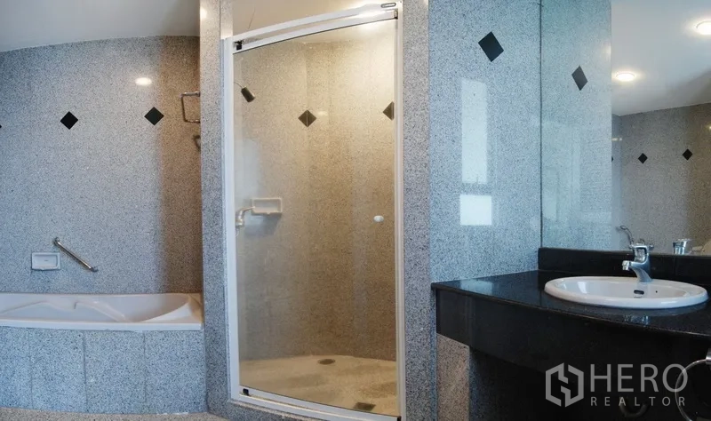 Condominium for rent in Watthana, Bangkok - Granite-tiled bathroom with bathtub, glass shower enclosure, and wide vanity.
