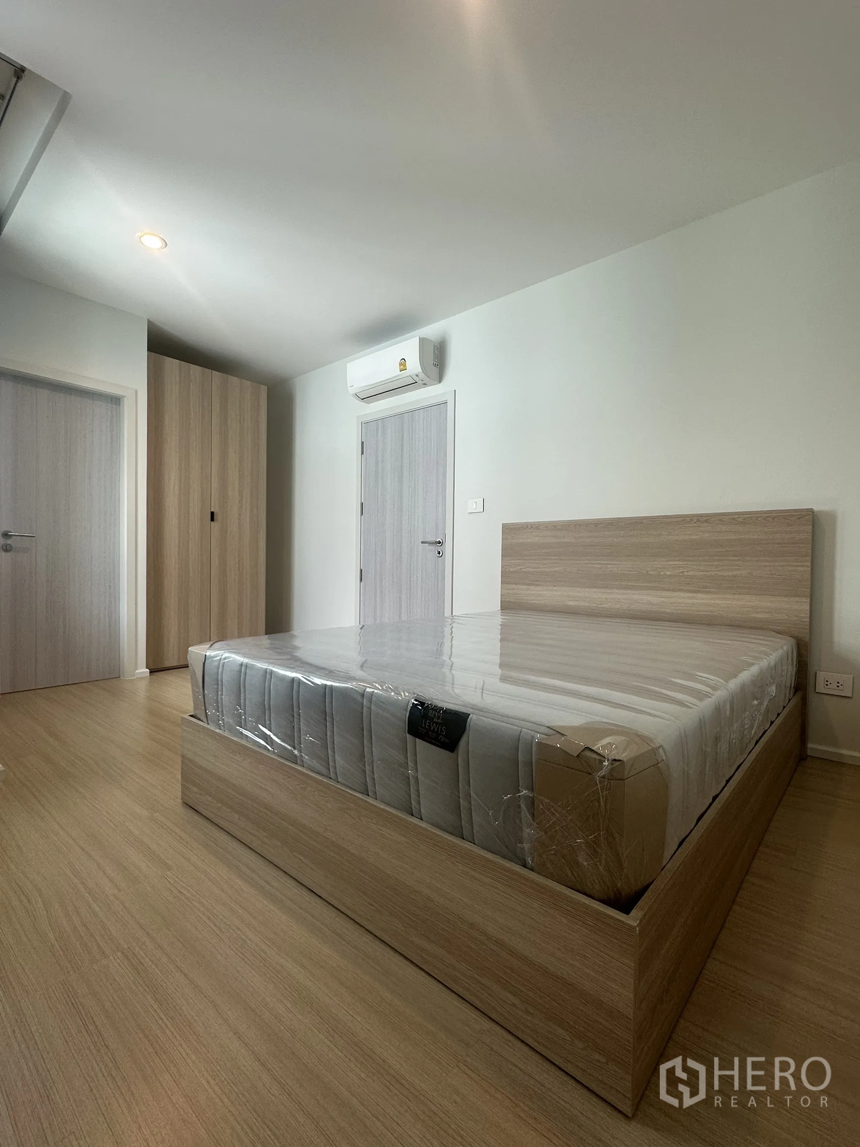Townhouse for rent in Suan Luang, Bangkok - Bedroom with a wood bed frame and new mattress near wardrobes and an air-conditioner.