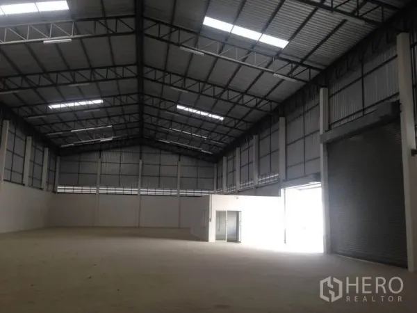 Warehouse for rent in Bang Bua Thong, Nonthaburi - Spacious warehouse interior with high steel truss roof, skylights and tall roller door.