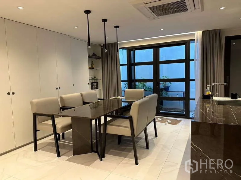 Townhouse for rent in Yan Nawa, Bangkok - Dining area with pendant lights beside patio-style windows and shelves.