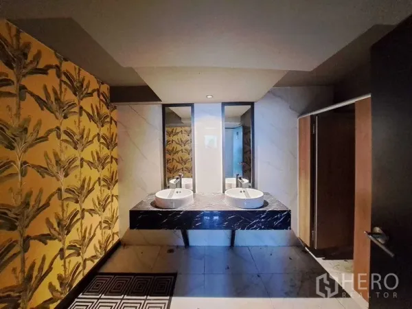 零售空间 出租在Watthana, Bangkok - 卫生间配双台上盆、黑色大理石台面、镜面与热带图案墙面。