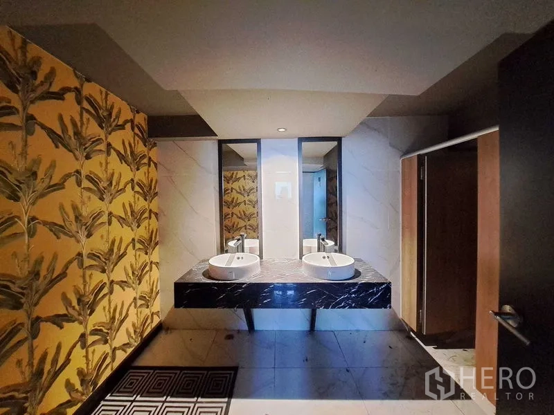 零售空间 出租在Watthana, Bangkok - 卫生间配双台上盆、黑色大理石台面、镜面与热带图案墙面。