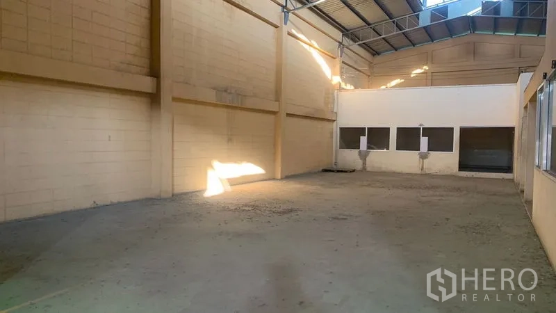 Warehouse for rent in Mueang Nakhon Pathom, Nakhon Pathom - Clean storage zone with tall walls, concrete floor, and two wall-mounted sinks at the rear.