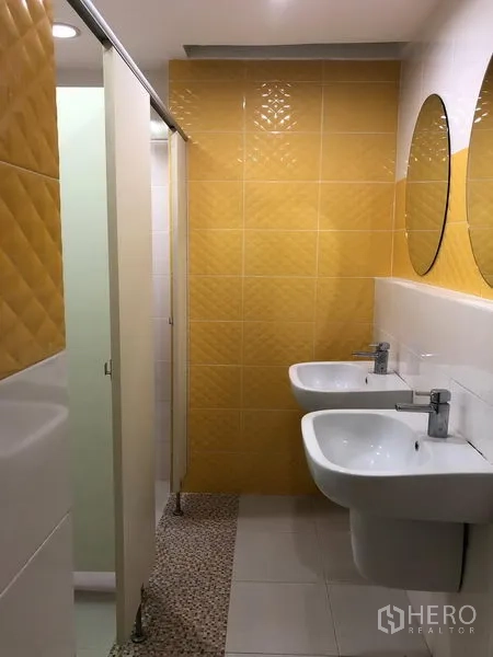 办公空间 出租在Bang Na, Bangkok - 现代化卫生间，黄色墙砖、双盆洗手台和独立隔间。