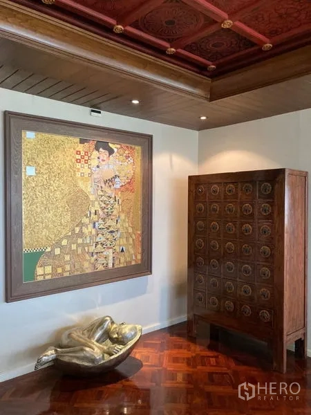 Condominium for rent in Bang Rak, Bangkok - Art-filled corner with gilded painting, ornate wooden cabinet, and patterned wood ceiling on polished floors.