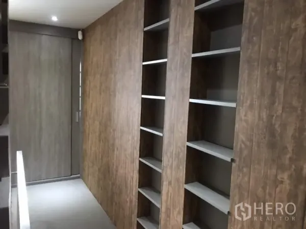 Townhouse for rent or sale in Suan Luang, Bangkok - Upper corridor with recessed lighting and floor-to-ceiling wood-paneled shelving and cabinets.