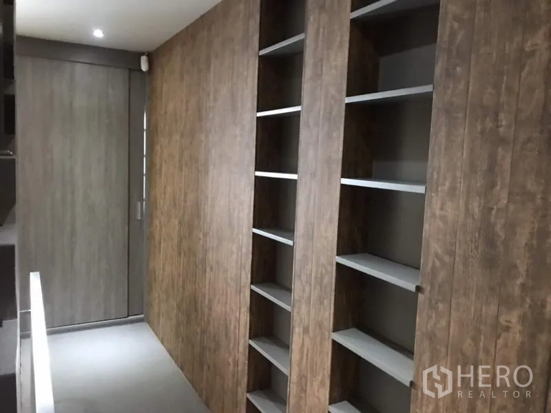 Townhouse for rent or sale in Suan Luang, Bangkok - Upper corridor with recessed lighting and floor-to-ceiling wood-paneled shelving and cabinets.