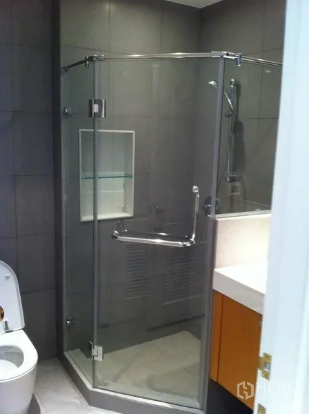 Condominium for rent in Pathum Wan, Bangkok - Modern bathroom featuring a glass-enclosed shower, gray wall tiles, vanity, and toilet.