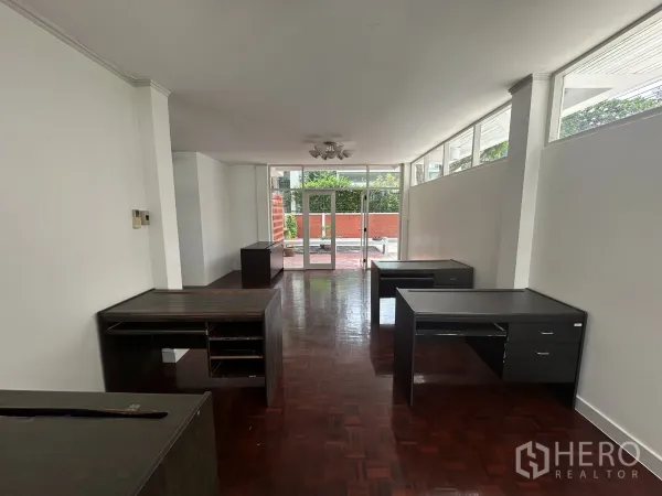 Home Office for rent in Watthana, Bangkok - Long workspace leading to glass doors opening to a front patio, dark wood desks arranged along walls.