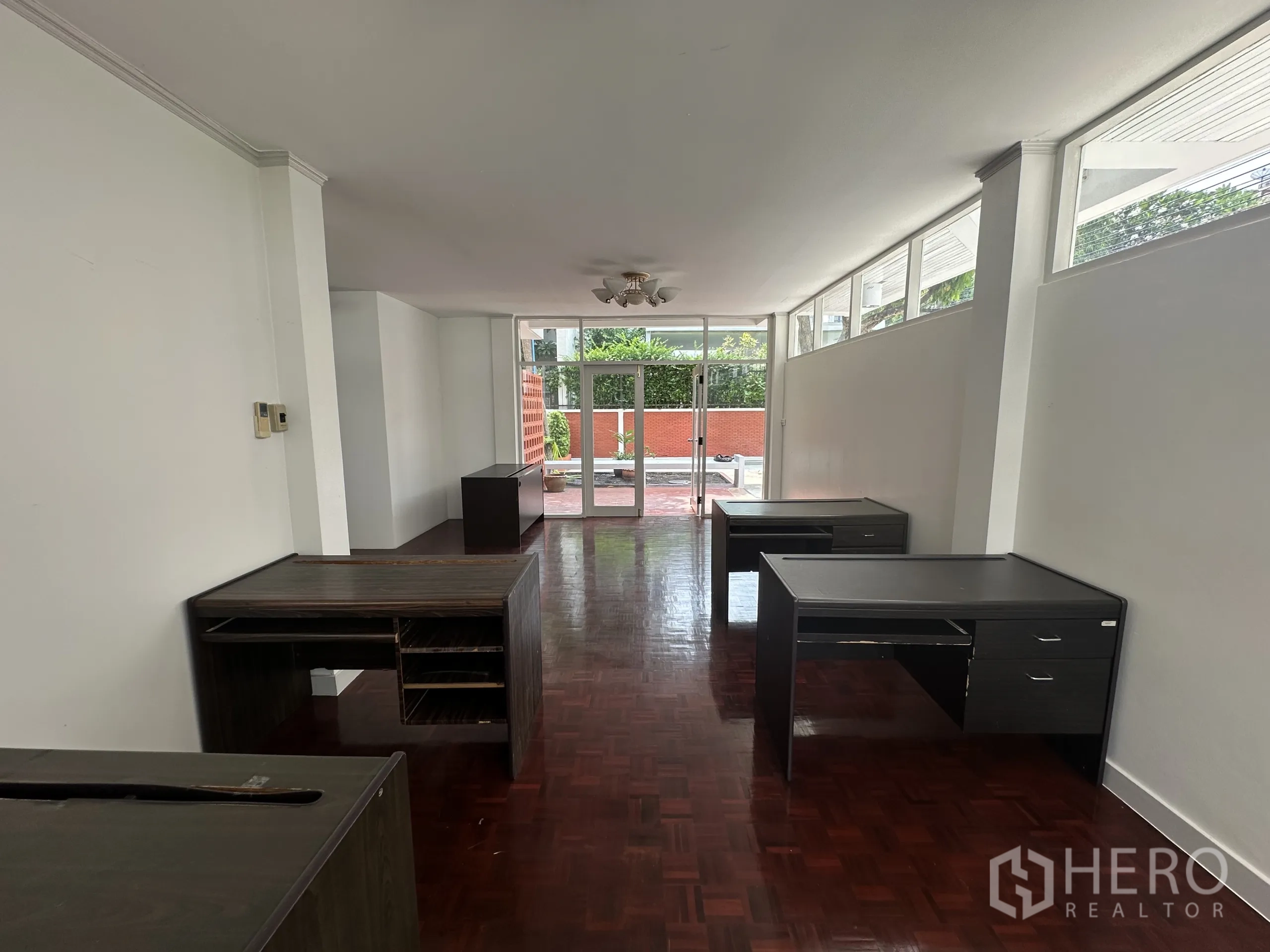 Home Office for rent in Watthana, Bangkok - Long workspace leading to glass doors opening to a front patio, dark wood desks arranged along walls.