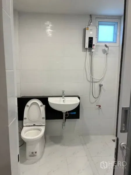 独立式住宅 出租在Samut Prakan - 明亮瓷砖浴室，配坐便器、洗手盆和壁挂式热水器花洒。