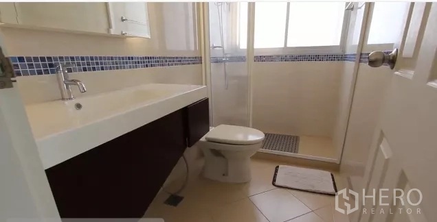 Condominium for rent in Watthana, Bangkok - Bathroom with glass-enclosed shower, vanity and toilet accented with blue mosaic tiles.