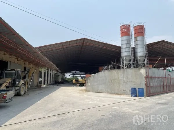 Factory for sale in Mueang Chon Buri, Chon Buri - Wide entrance yard showing tall twin silos and roofed bays.