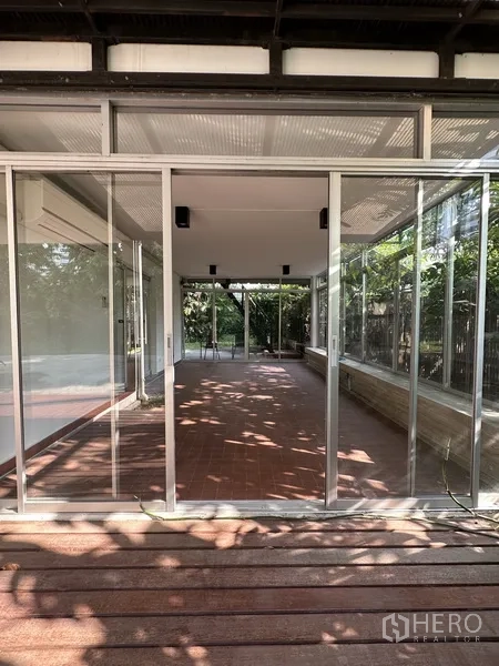 Detached House for rent in Khlong Toei, Bangkok - Glass‑enclosed terrace with red tile flooring and a wooden deck outside.