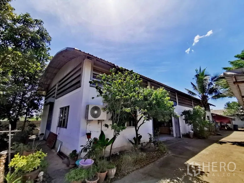 货栈 出售在Pathum Thani - 仓库外观，弧形金属屋顶与白色墙面，绿植与车道，蓝天之下。