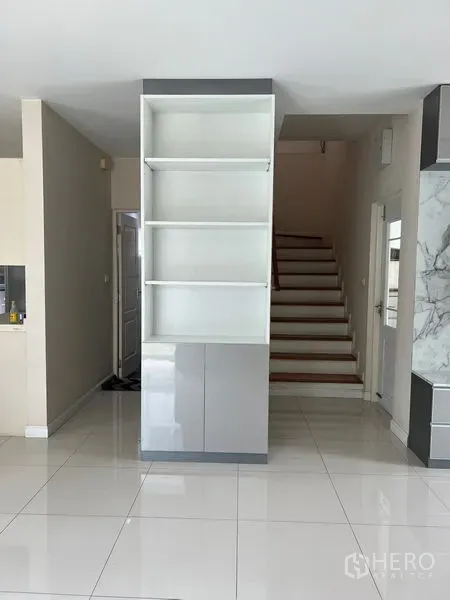 Detached House for rent in Bang Kapi, Bangkok - Hallway with glossy tile floors, built-in shelving, and staircase to the upper level.