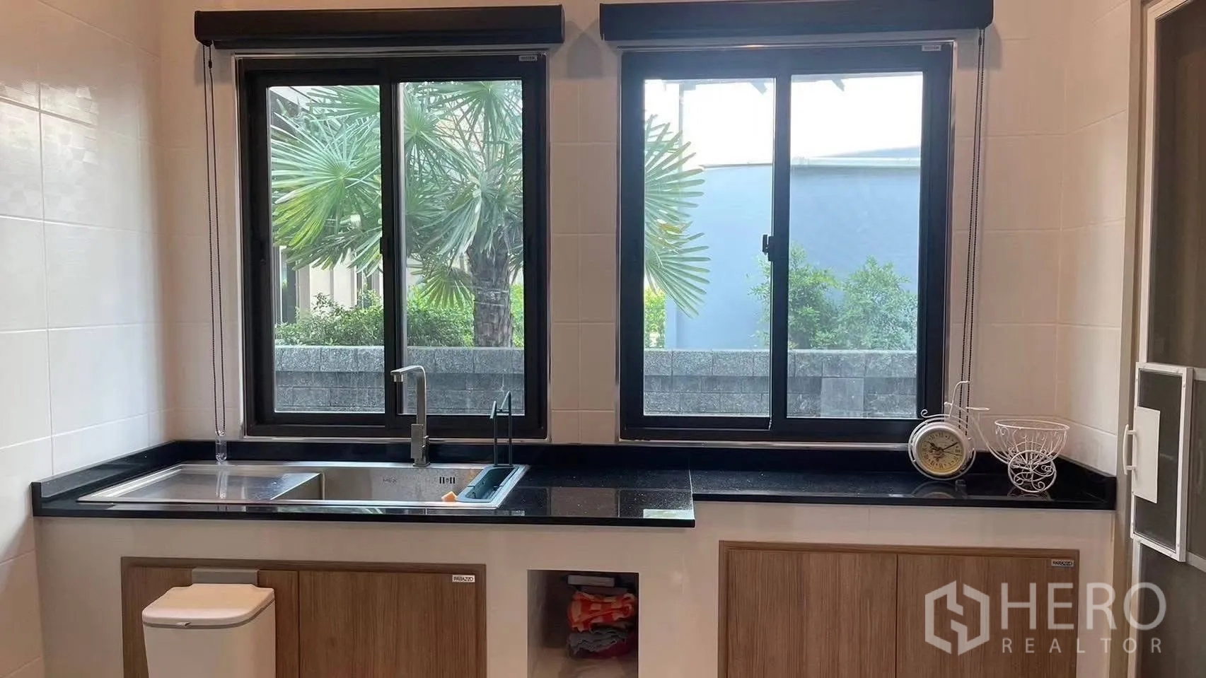 Detached House for rent in Prawet, Bangkok - Kitchen sink and black countertops beneath two sliding windows facing greenery.