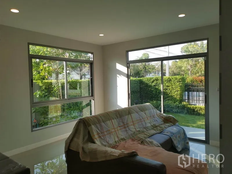 Detached House for sale in Nonthaburi - Corner living room with large sliding windows opening to a green garden.