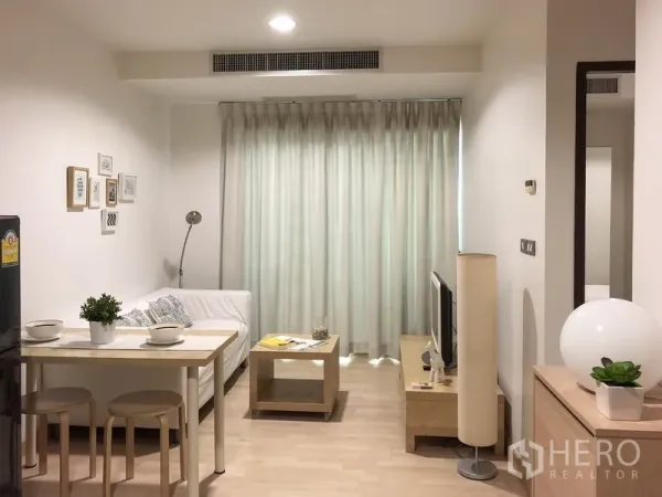 公寓 出租或出售在Watthana, Bangkok - 从入口望向客厅，见餐桌、沙发、电视柜、落地窗帘与中央空调出风口。