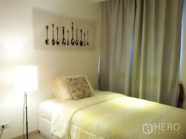 คอนโด ให้เช่าหรือขาย - ห้องนอนรองพร้อมเตียงเดี่ยว โคมไฟตั้งพื้น และผ้าม่านทึบแสง