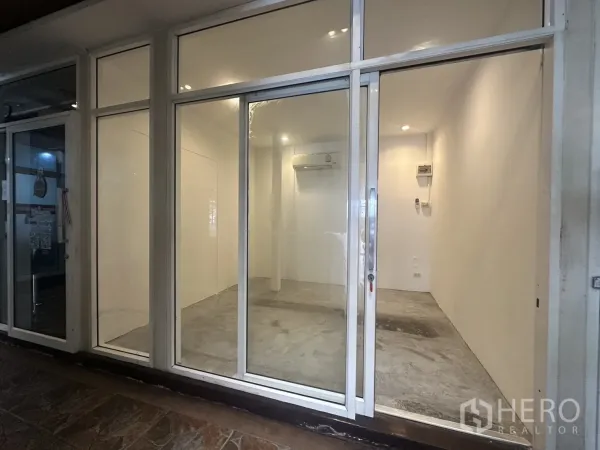 พื้นที่ขายปลีก ให้เช่า - หน้าร้านกระจกพร้อมประตูบานเลื่อน ผนังสีขาว พื้นคอนกรีต ไฟดาวน์ไลท์ และแอร์ ในคอมมิวนิตี้มอลล์ใกล้ BTS พร้อมพงษ์