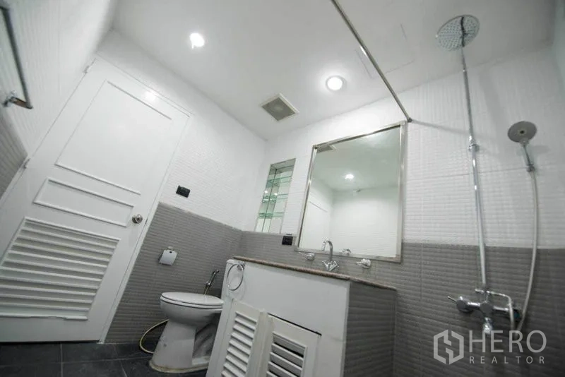 公寓 出租在Khlong Toei, Bangkok - 紧凑浴室，雨淋花洒，白灰墙砖，配洗手台与坐便器。