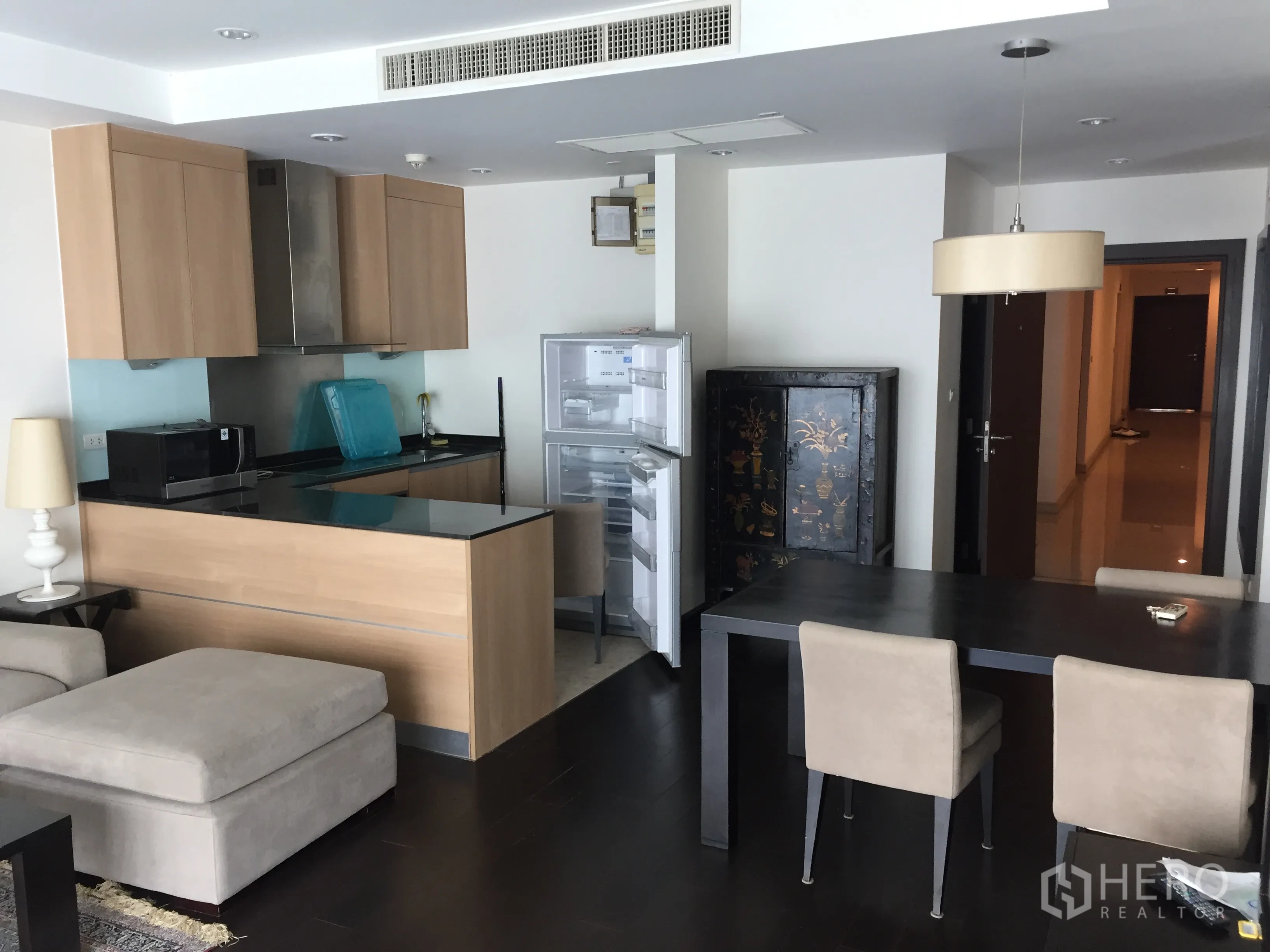 公寓 出租在Sathon, Bangkok - 开放式空间，木色橱柜的厨房与吧台，旁有餐桌和打开的冰箱。