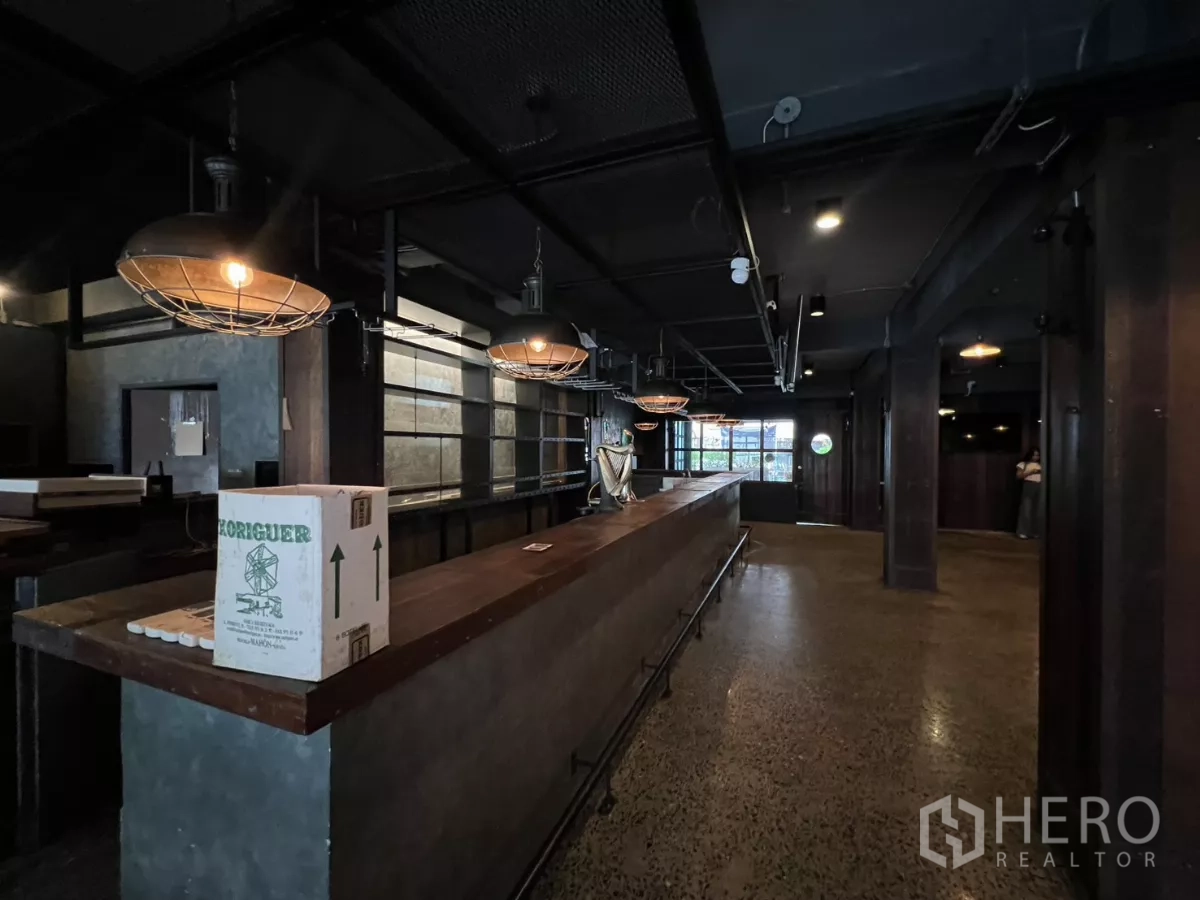 零售空间 出租 - 开放空间中的加长木吧台与金属护笼吊灯。